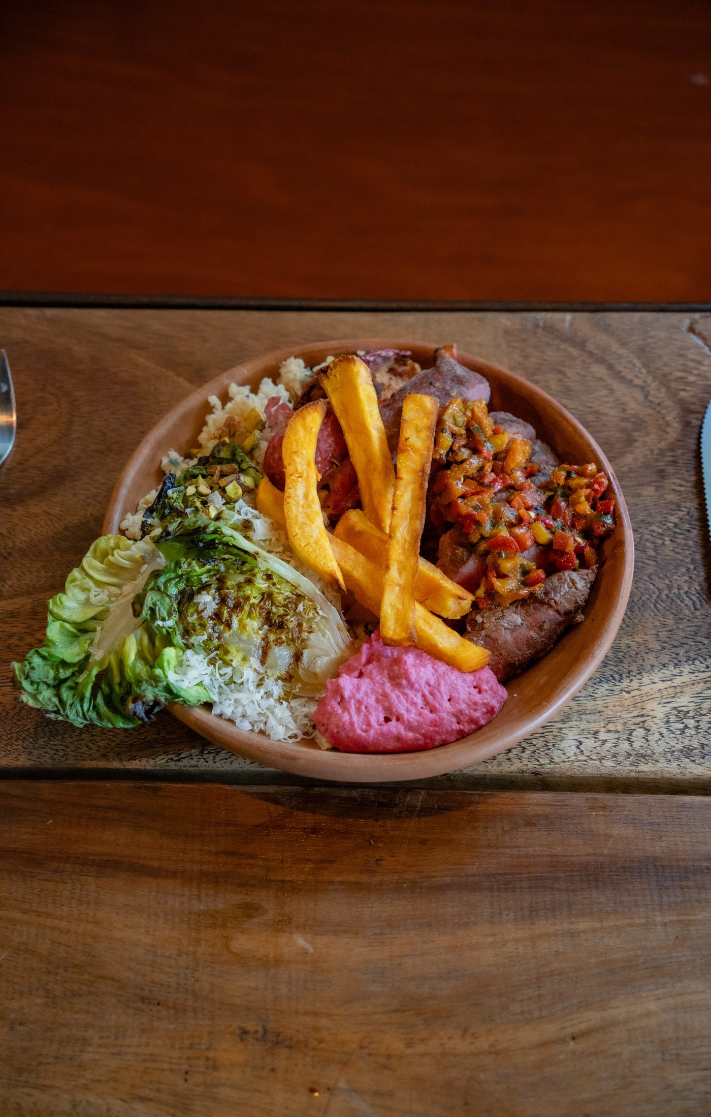 Bowl Kieto: vacío, papas de camote, ensalada y salsa sobre mesa de madera